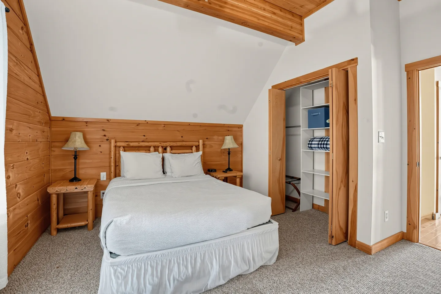 Bedroom with a bed, log-style headboard and nightstands, angled ceiling with wood trim, and an open closet.