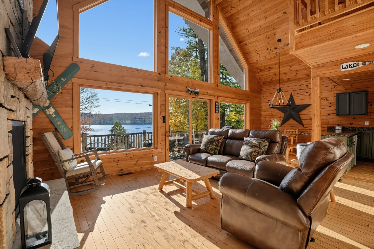 Living room with wood walls and ceiling, leather seating, and large windows overlooking a lake.