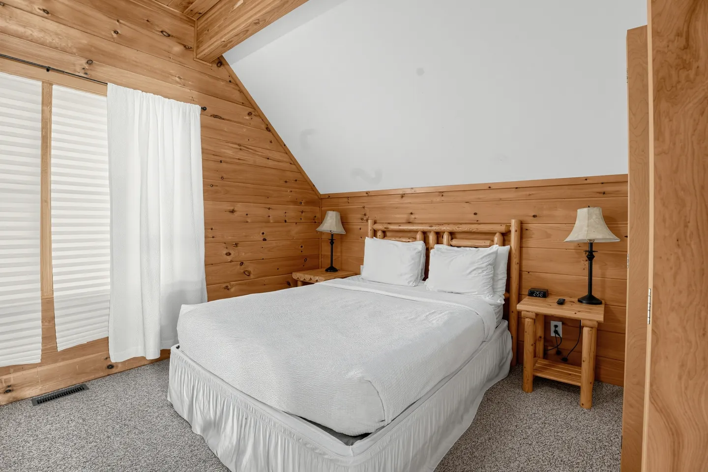 Bedroom with wood-paneled walls, a vaulted ceiling, and a log-frame bed with white bedding.
