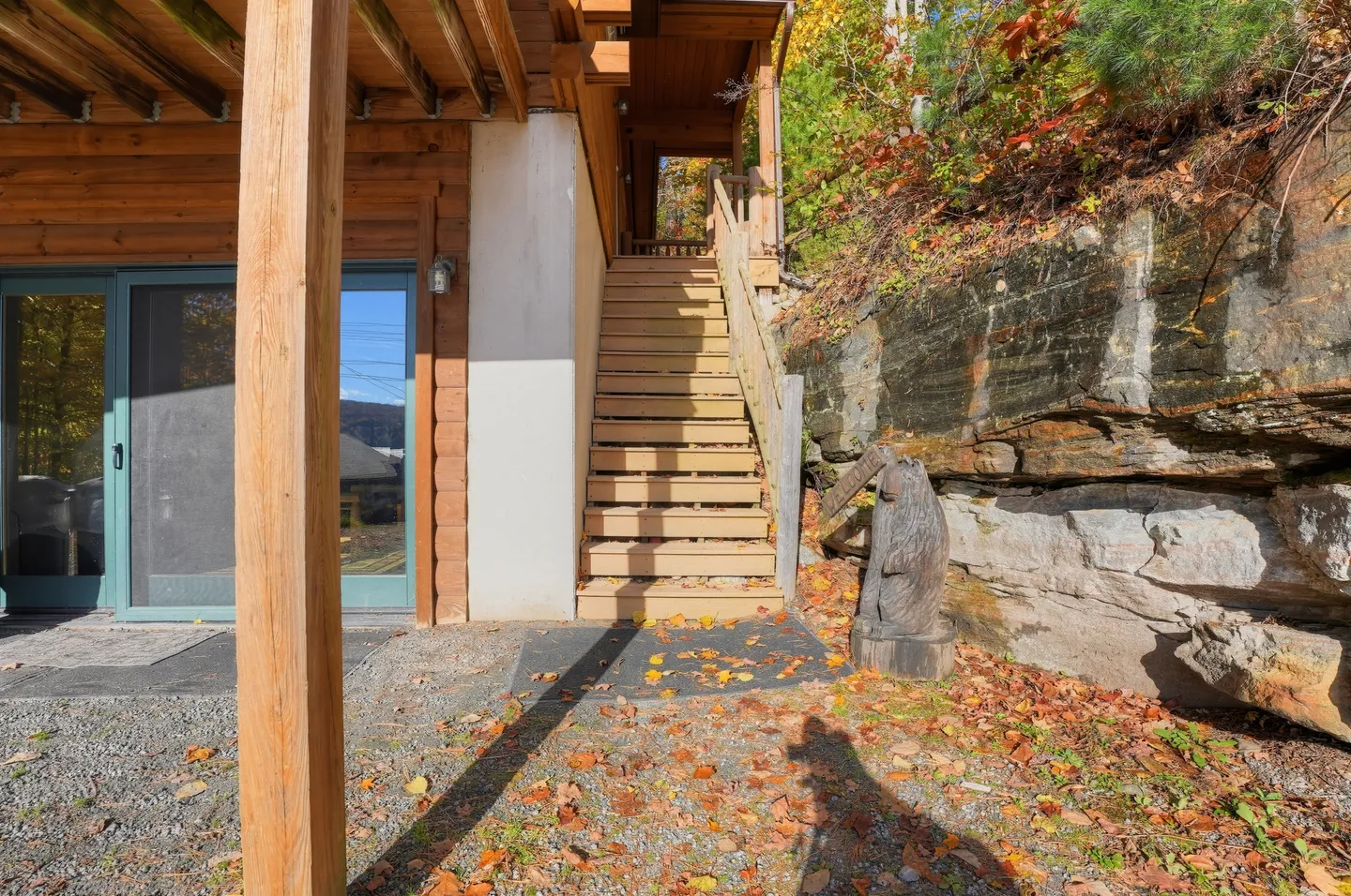 Exterior wooden staircase leading to an upper deck alongside a rock face with a carved wooden bear statue at the base.