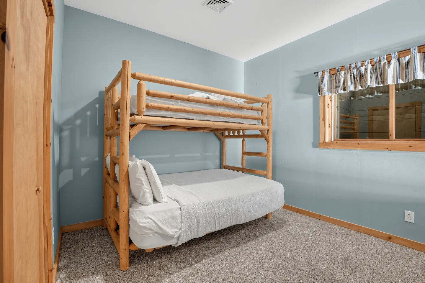 Bedroom with blue walls, carpeted floor, and a wooden log bunk bed with white linens.