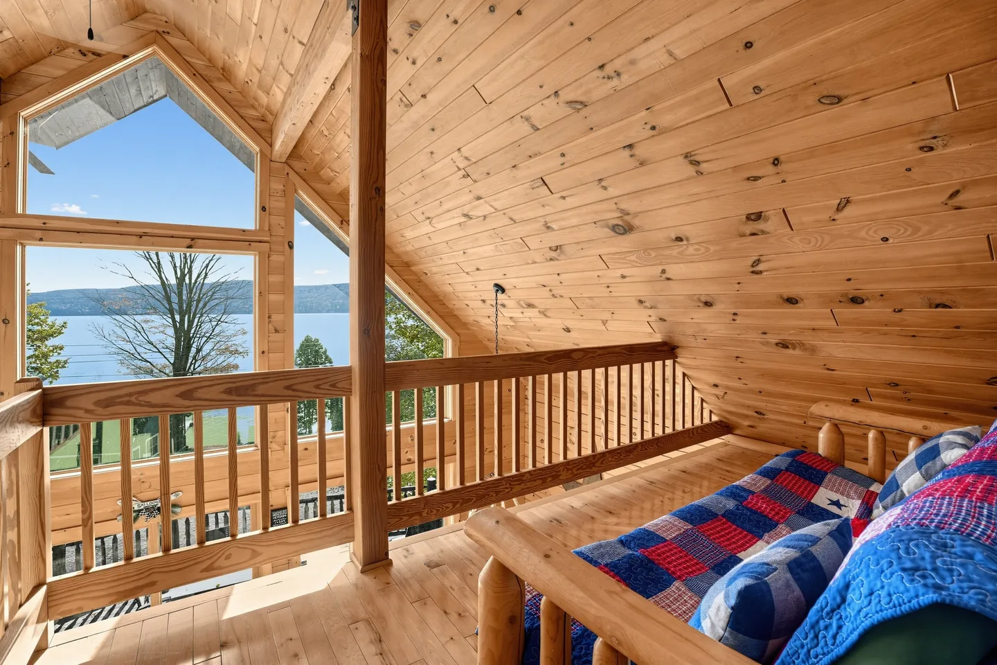 A wood-paneled loft with a log daybed overlooking large windows that offer views of a lake and trees.