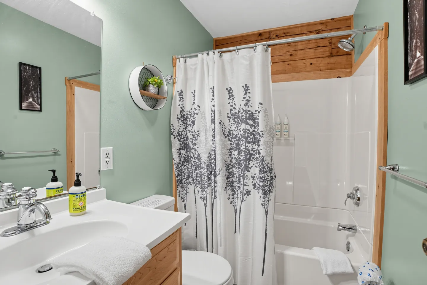 Bathroom with a vanity, toilet, and bathtub-shower combination with a tree-patterned curtain.