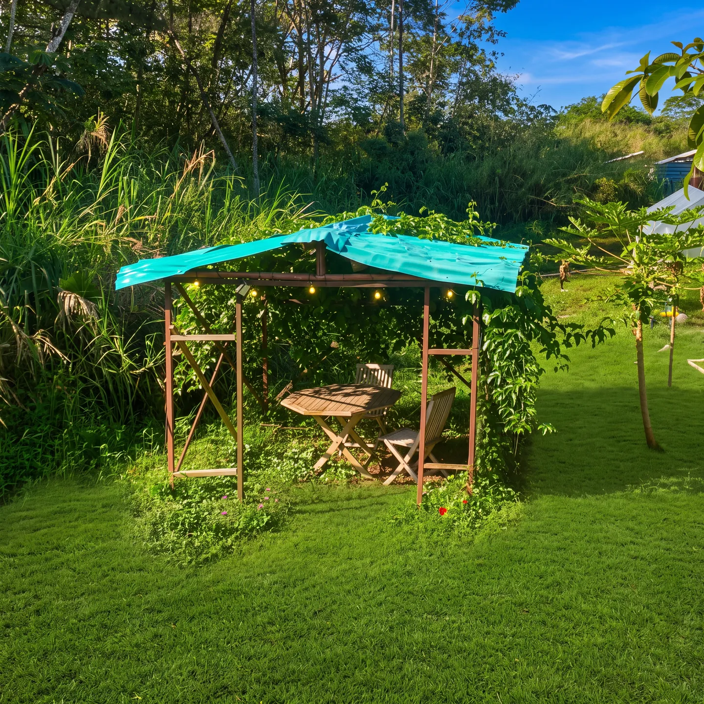A small covered wooden gazebo with a table and chairs on a grassy lawn surrounded by lush greenery.