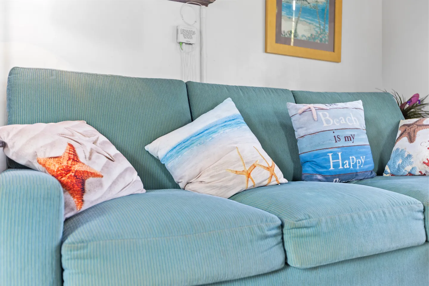A close-up view of a light blue sofa with coastal-themed throw pillows against a white wall.