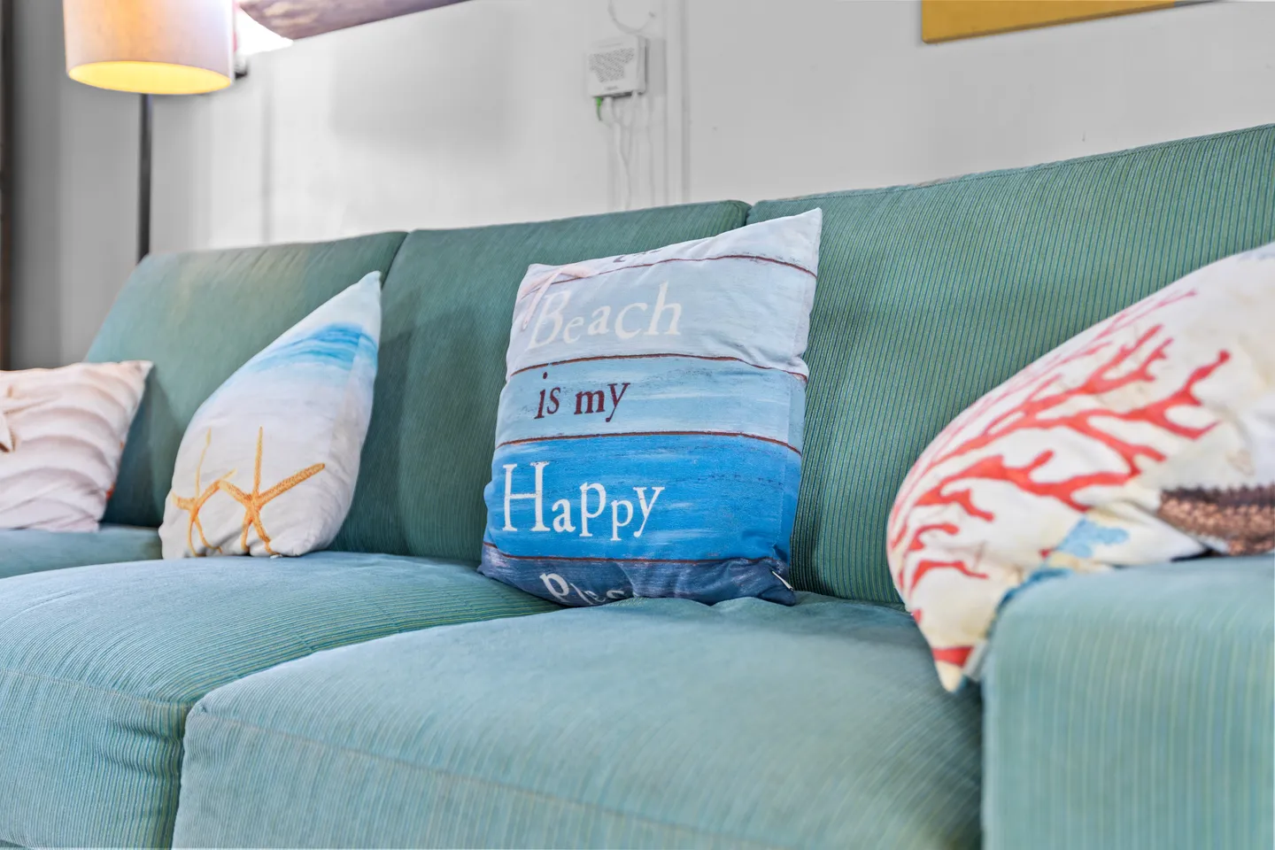 Close-up of a teal corduroy sofa decorated with coastal-themed throw pillows and a floor lamp in the background.