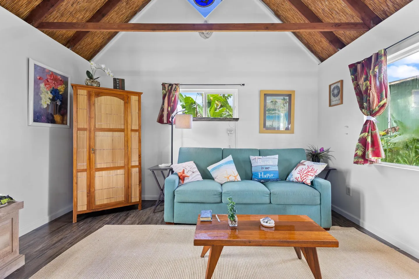 Living area with a turquoise sofa, wooden coffee table, large armoire, and vaulted ceiling with exposed wooden beams.