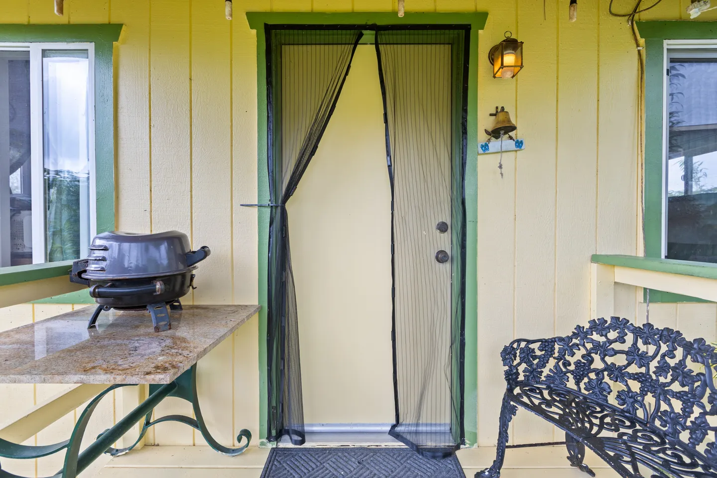 Exterior doorway with a magnetic mesh screen door, flanked by a grill on a table and a wrought-iron bench on the porch.