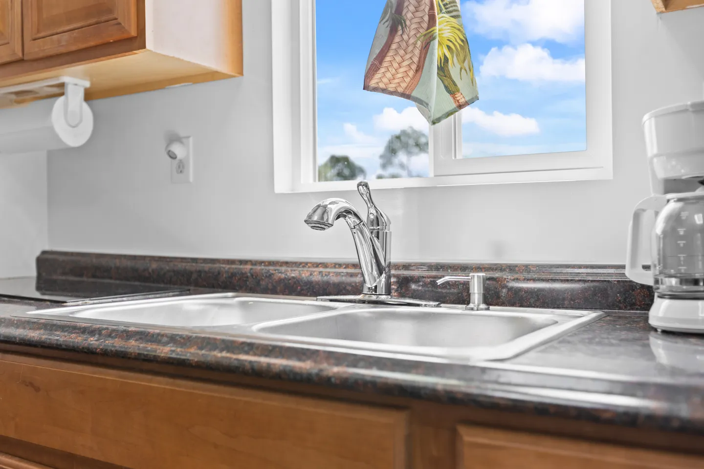 Close-up of a kitchen double sink with a chrome faucet beneath a window showing blue sky and clouds.
