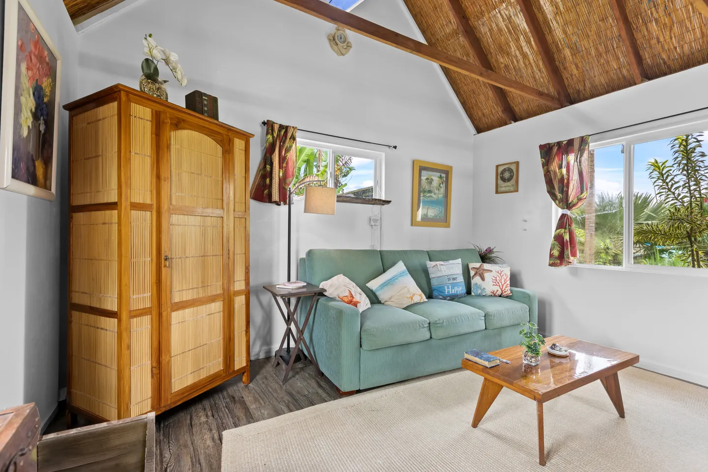 Living area featuring a teal sofa with throw pillows, wooden coffee table, large armoire, and vaulted ceiling with thatched texture.