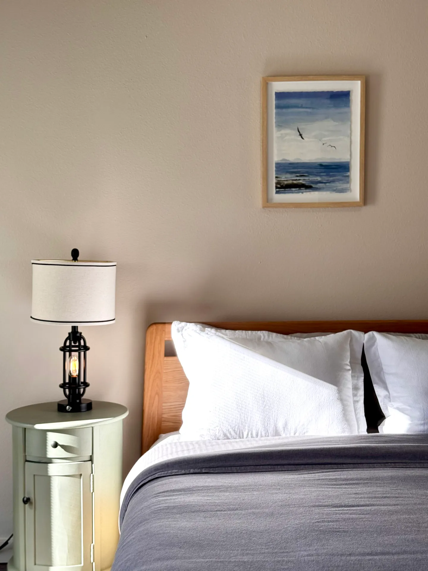 Bedroom detail featuring a wooden bed, white pillows, a nightstand with a lamp, and framed artwork on the wall.
