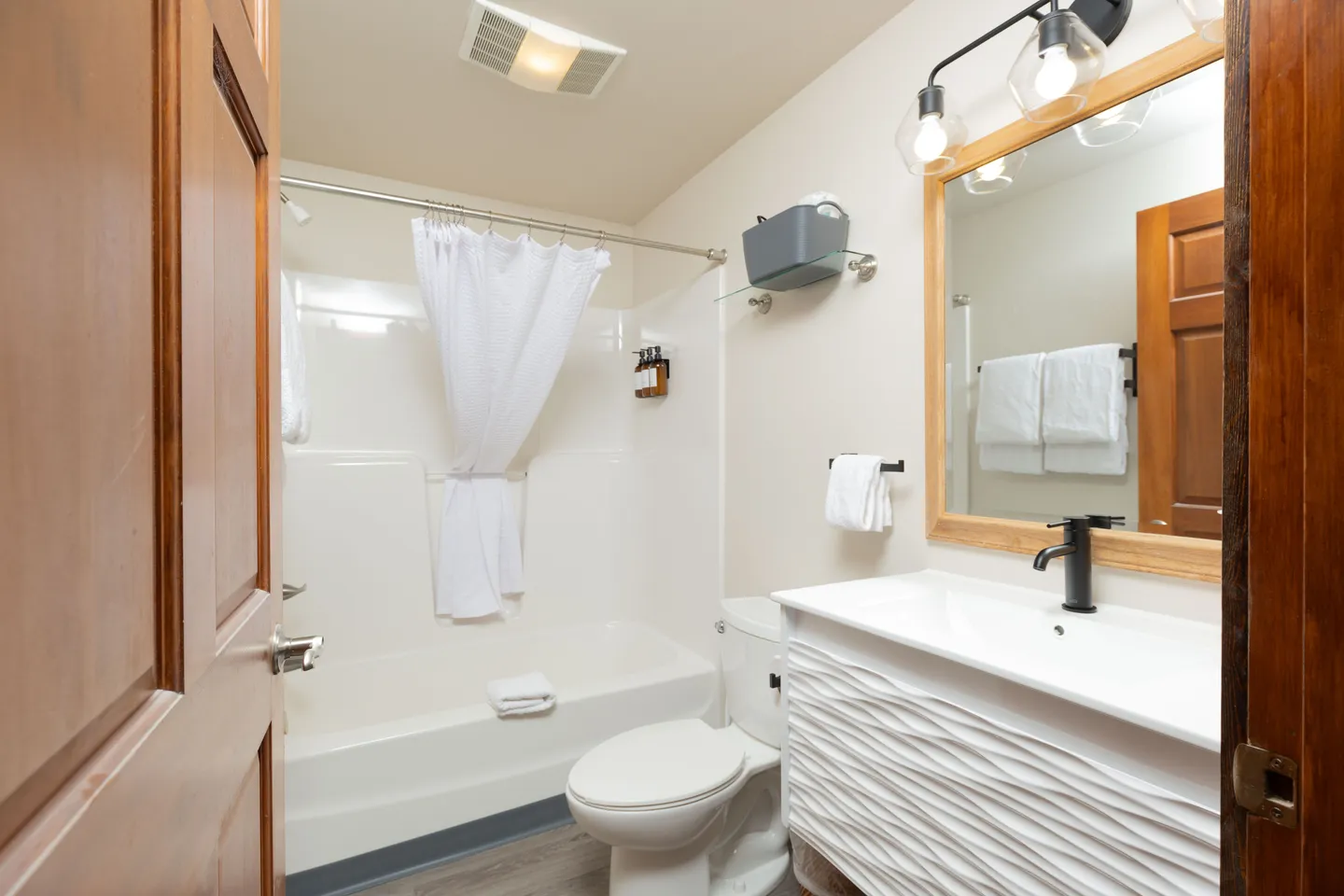 Bathroom with white textured vanity, toilet, and combination shower tub with white curtain.