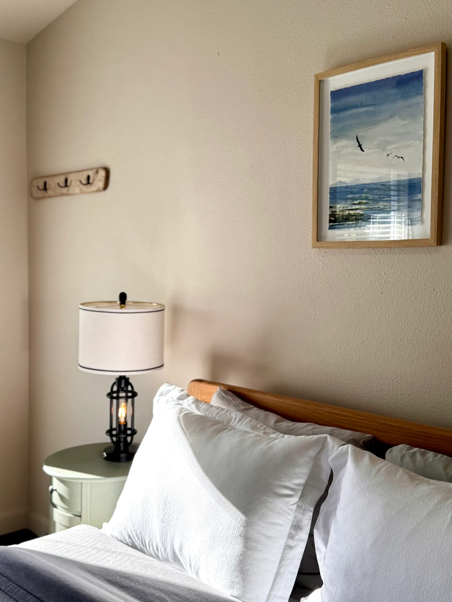 Close-up of a bed with white pillows and a wooden headboard next to a nightstand with a lamp.