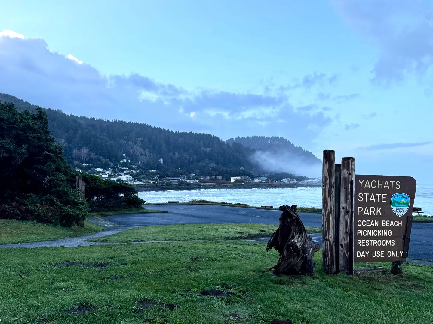 Sign for Yachats State Park in Oregon overlooking an ocean bay and forested hills.