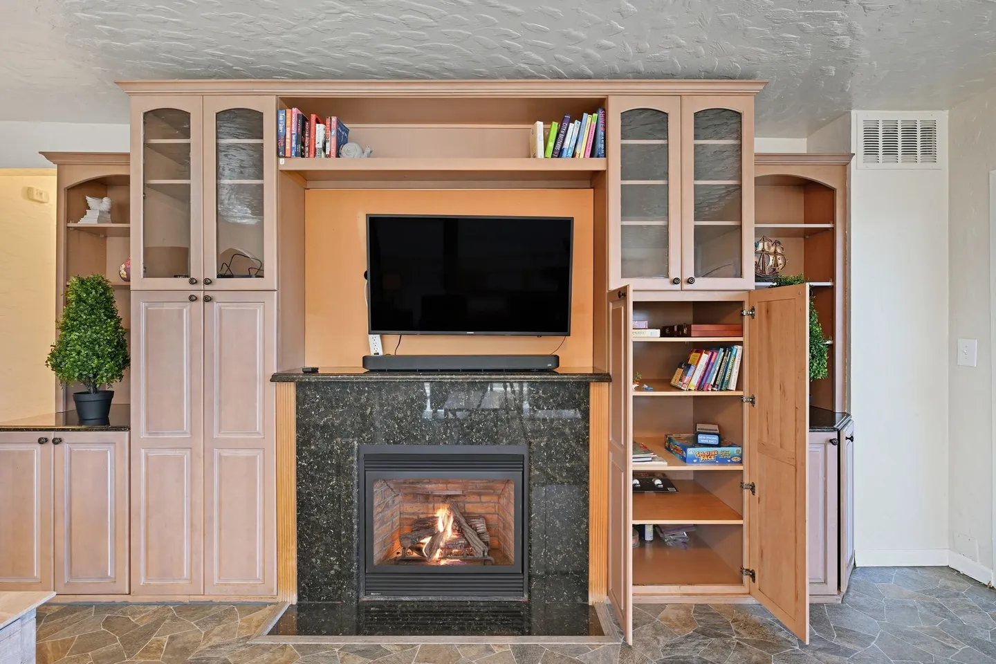A built-in wooden entertainment center with a lit fireplace, mounted flat-screen TV, and surrounding shelving and cabinetry.