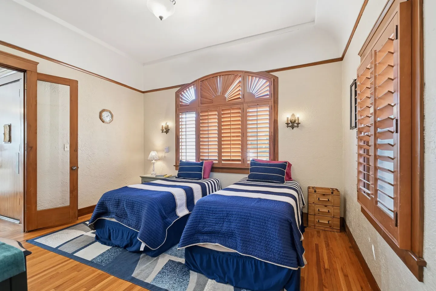Bedroom with two twin beds dressed in blue and white bedding, wooden floors, and plantation shutters.