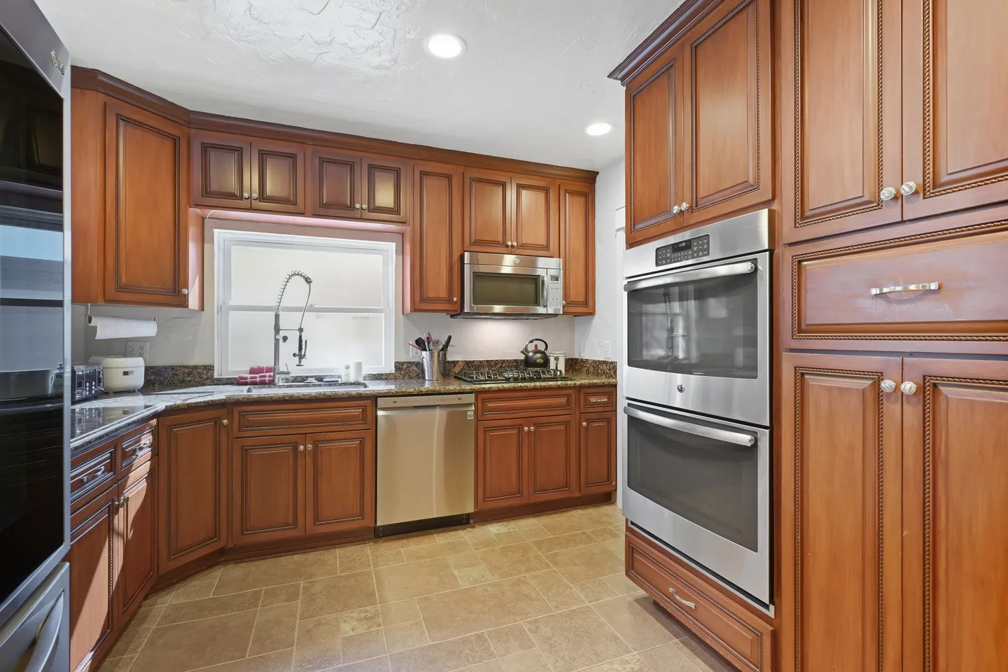 Kitchen with wooden cabinetry, stainless steel double wall ovens, dishwasher, and granite countertops.
