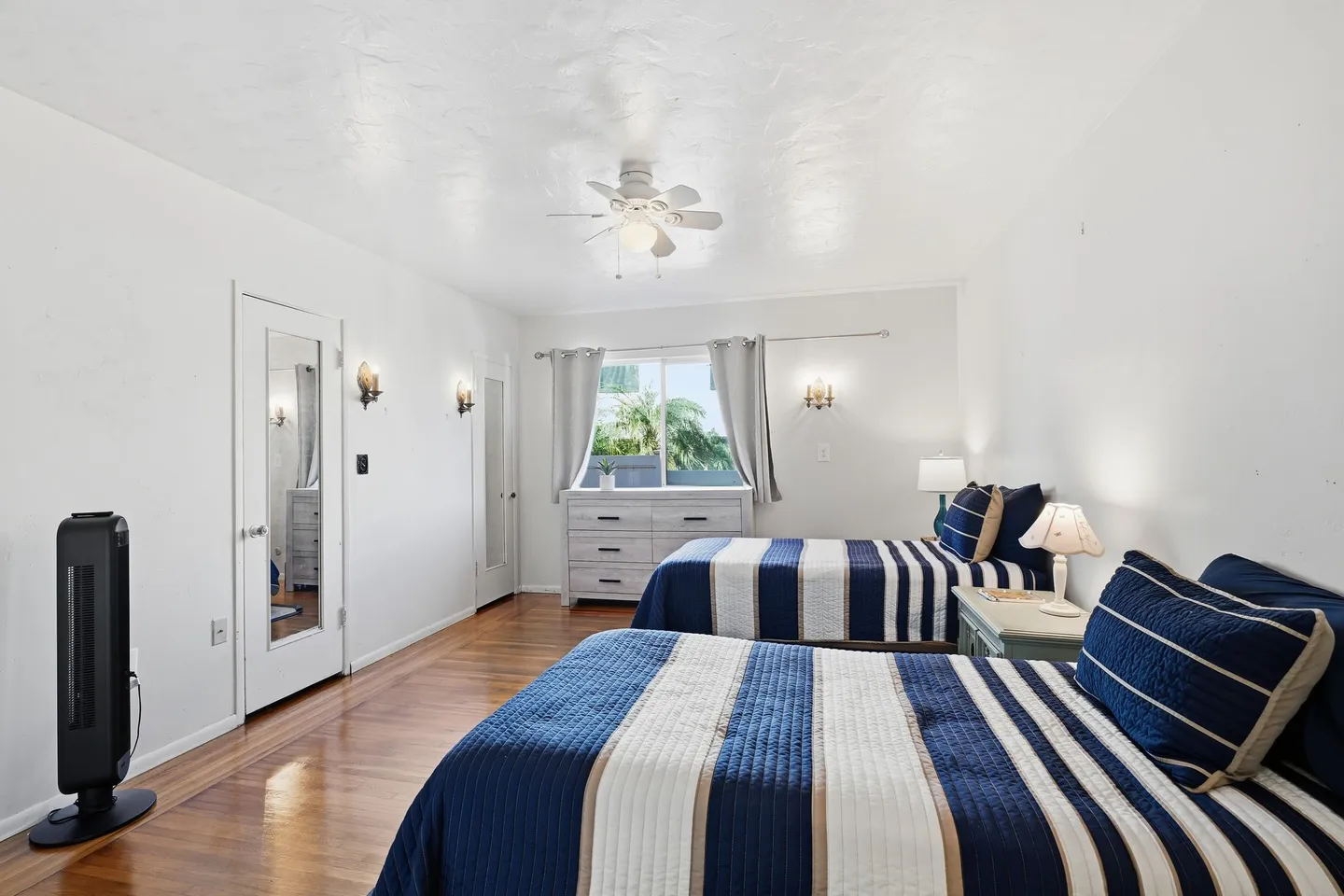 Bedroom with two beds made with blue and white striped bedding, wood-look flooring, and a ceiling fan.