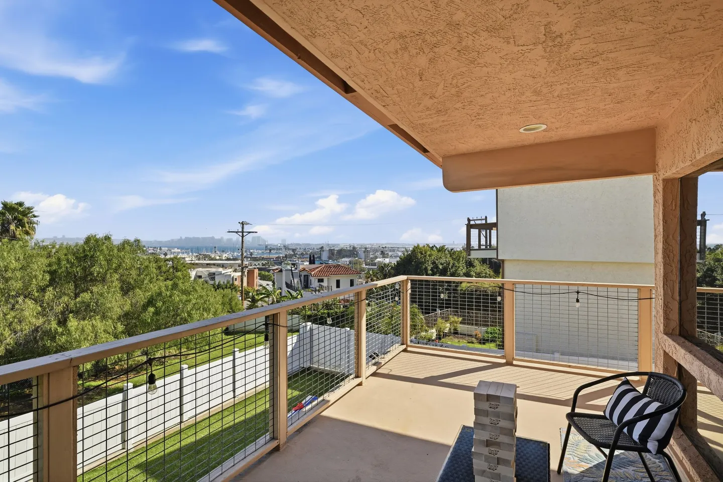 Elevated outdoor balcony with wire railing, outdoor chair, and a view of the surrounding neighborhood and distant water.
