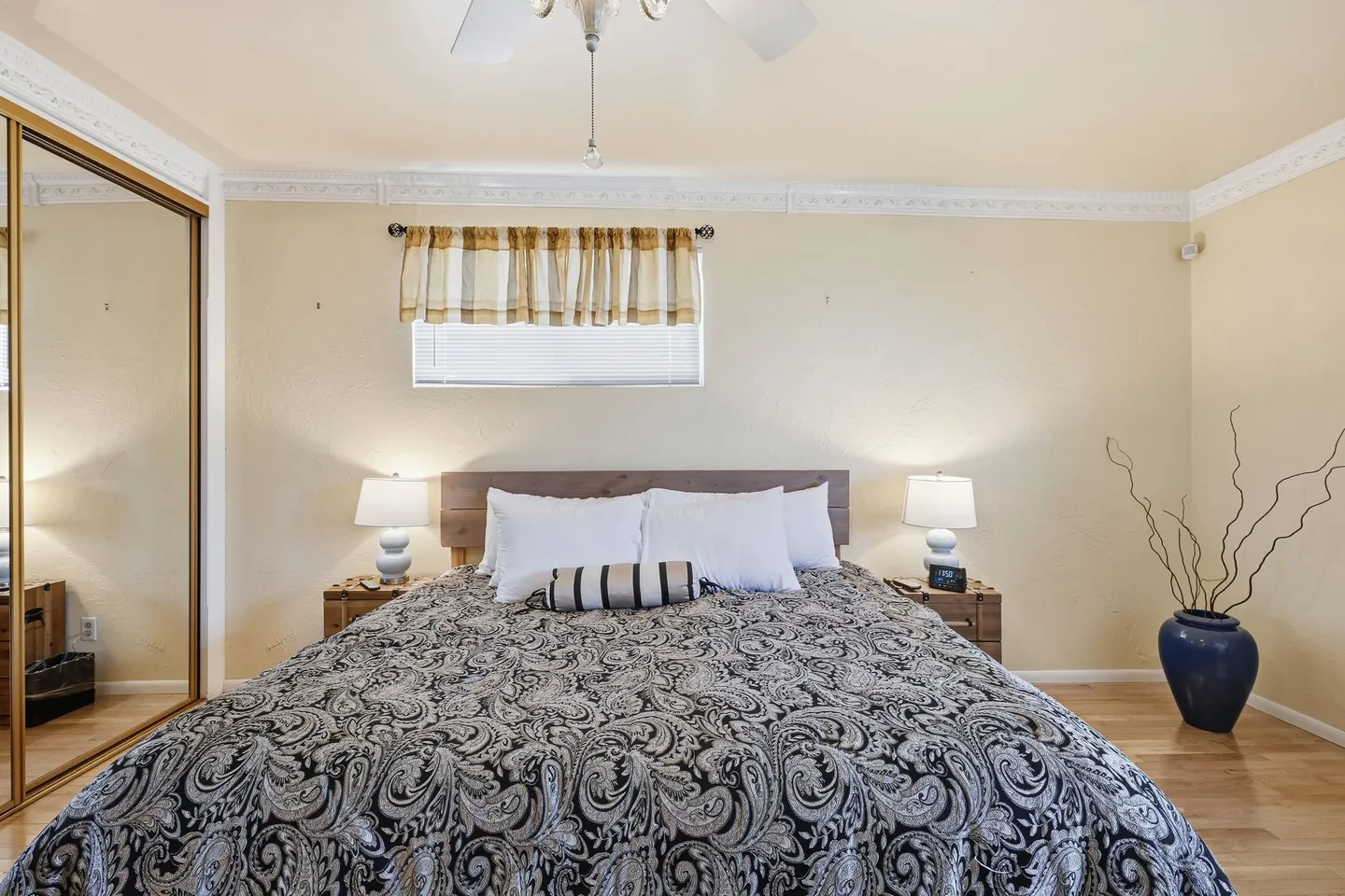 Bedroom featuring a made bed with a patterned comforter, two bedside tables with lamps, mirrored closet doors, and light yellow walls.