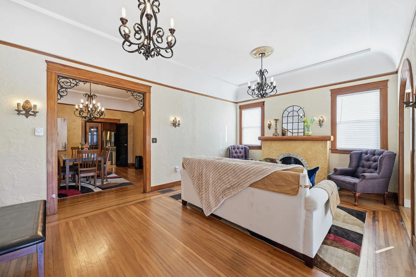 Living room with hardwood floors, a white sofa draped with blankets, a fireplace, and a wide doorway opening to the dining room.