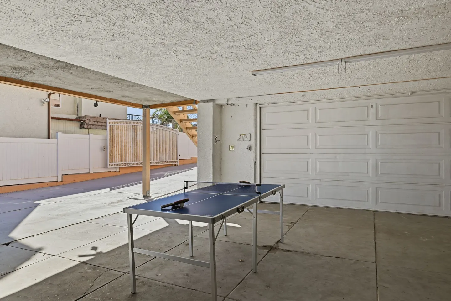 A ping pong table set up in a covered outdoor patio area next to a white garage door.