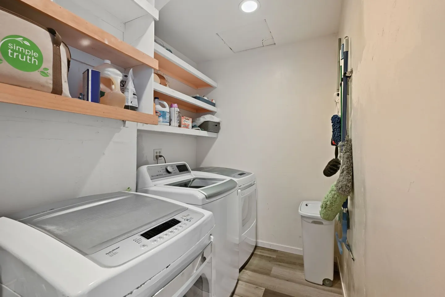 Dedicated indoor laundry room with a white washer and dryer, open shelving, and cleaning supplies.