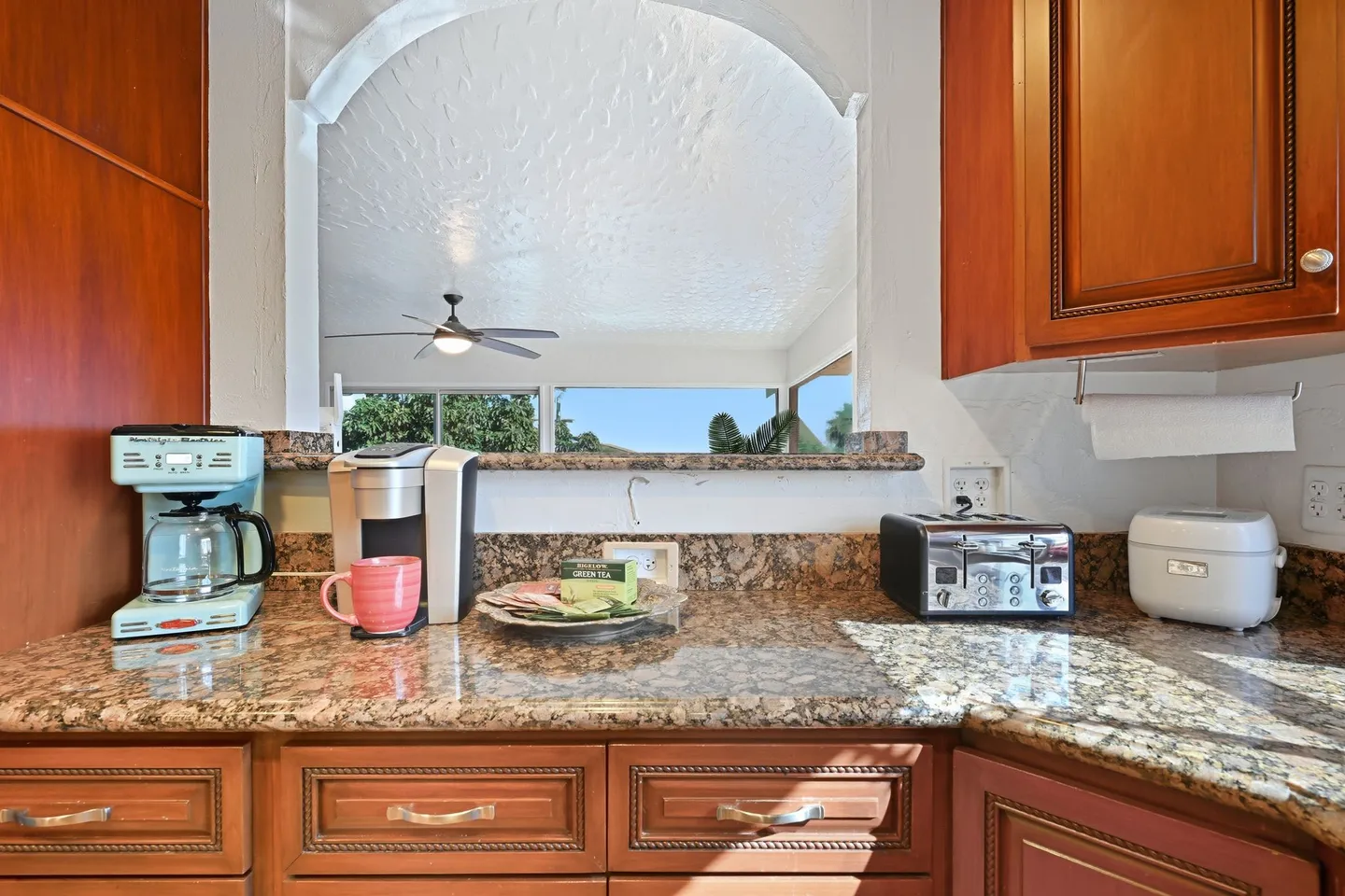 Kitchen counter nook with coffee makers, a toaster, and an arched pass-through window looking into an adjacent room.