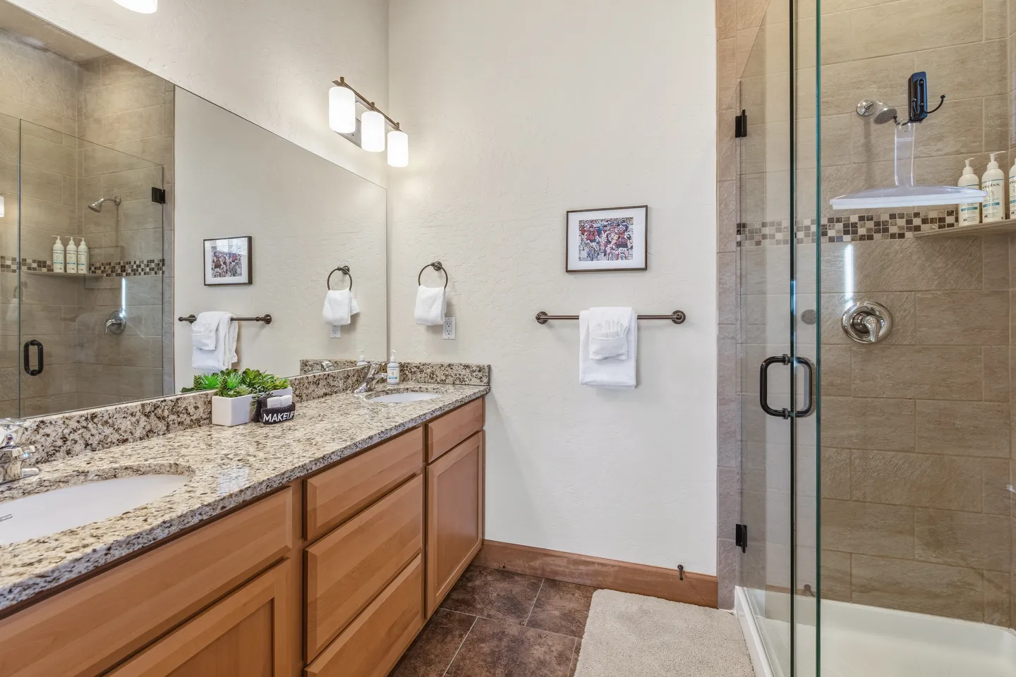 Bathroom featuring a double vanity with granite countertop and a glass-enclosed walk-in shower with tiled walls.
