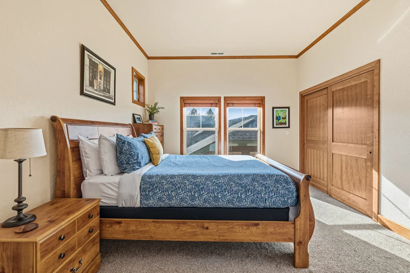 Bedroom with a wood sleigh bed, nightstand with lamp, carpeted floor, wood-framed windows, and wooden closet doors.