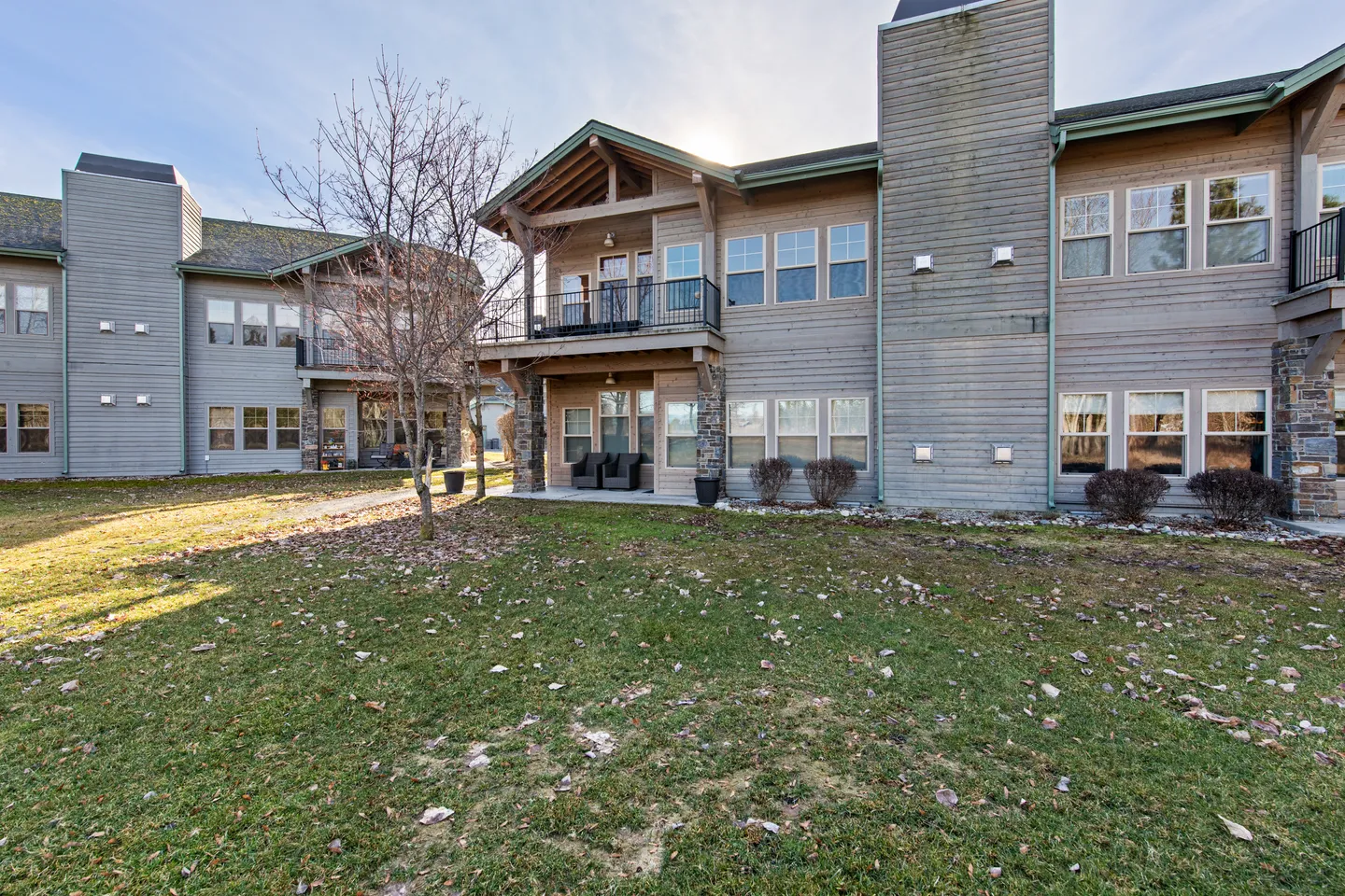 Exterior view of a multi-unit residential building with wood-look siding, stone accents, balconies, and a grassy lawn.