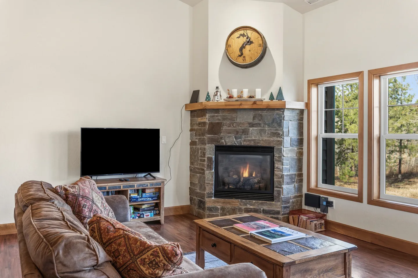 Living room corner featuring a stone fireplace, wood coffee table, TV stand with games, and a plush sofa.