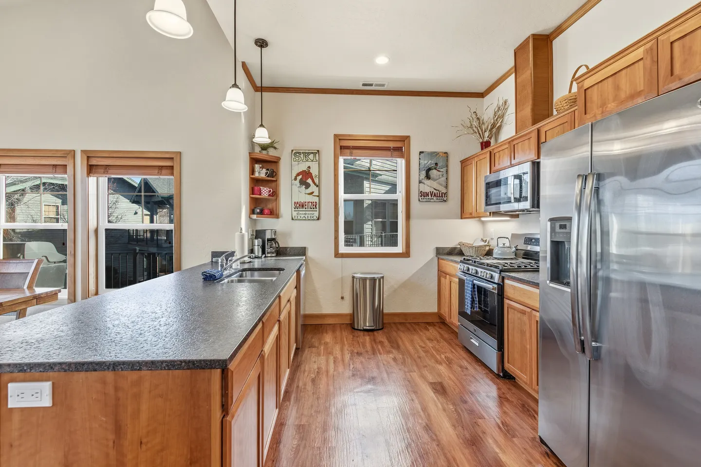 Kitchen with wood cabinetry, dark countertops, an island with a sink, stainless steel appliances, and wood flooring.