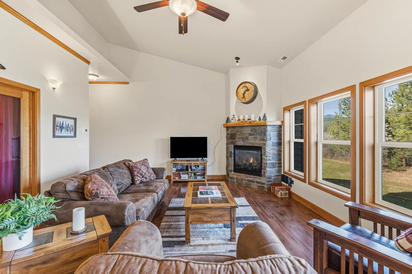 Living room with a stone corner fireplace, brown leather sofa, coffee table, and large windows.
