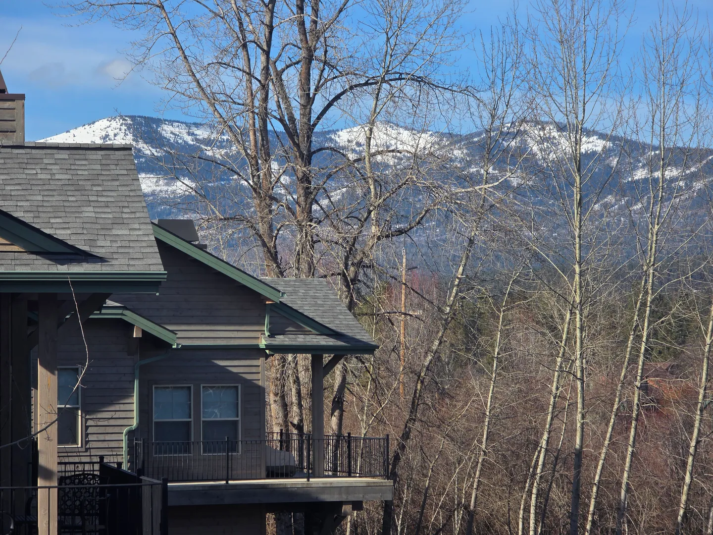 Exterior corner of a multi-story home with a balcony railing, bare trees, and snow-dusted mountains in the distance.