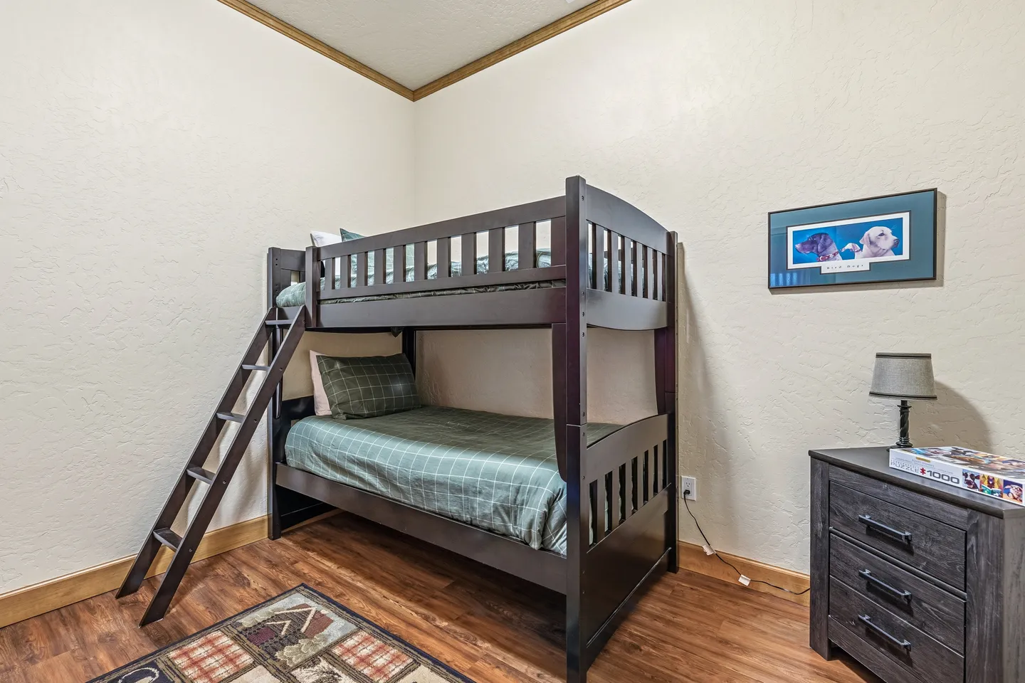 Bedroom corner with dark wood bunk beds, an angled access ladder, a small nightstand with a lamp, and wood-look flooring.