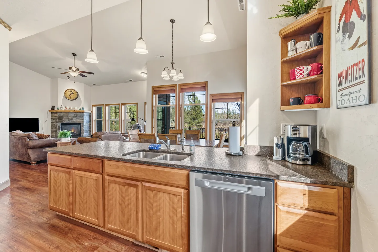 Open-concept kitchen island with a double sink and stainless steel dishwasher looking toward the dining area and living room.