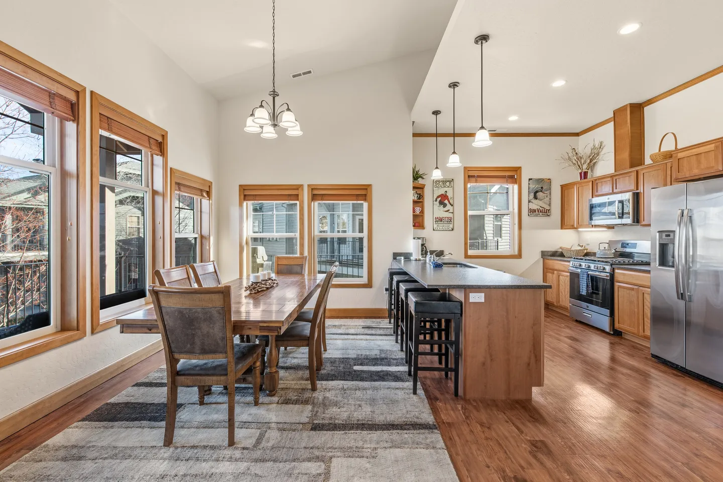 Open-concept dining area and kitchen with wood table, breakfast bar with stools, and stainless steel appliances.