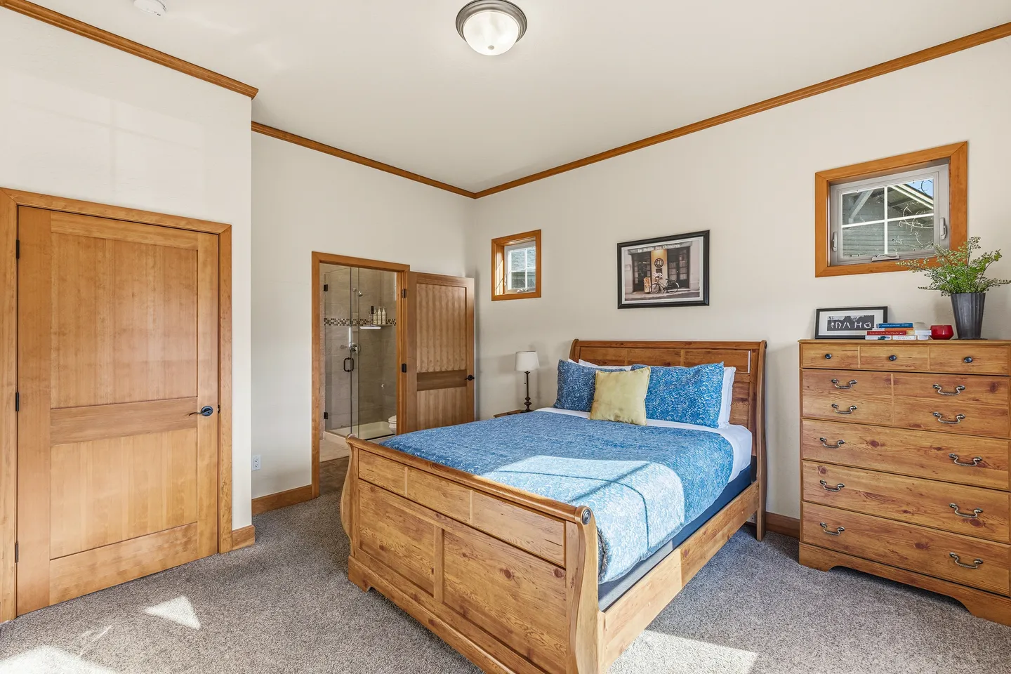 Bedroom with a wood sleigh bed, matching dresser, carpeted floor, and an open doorway leading into an en suite bathroom.