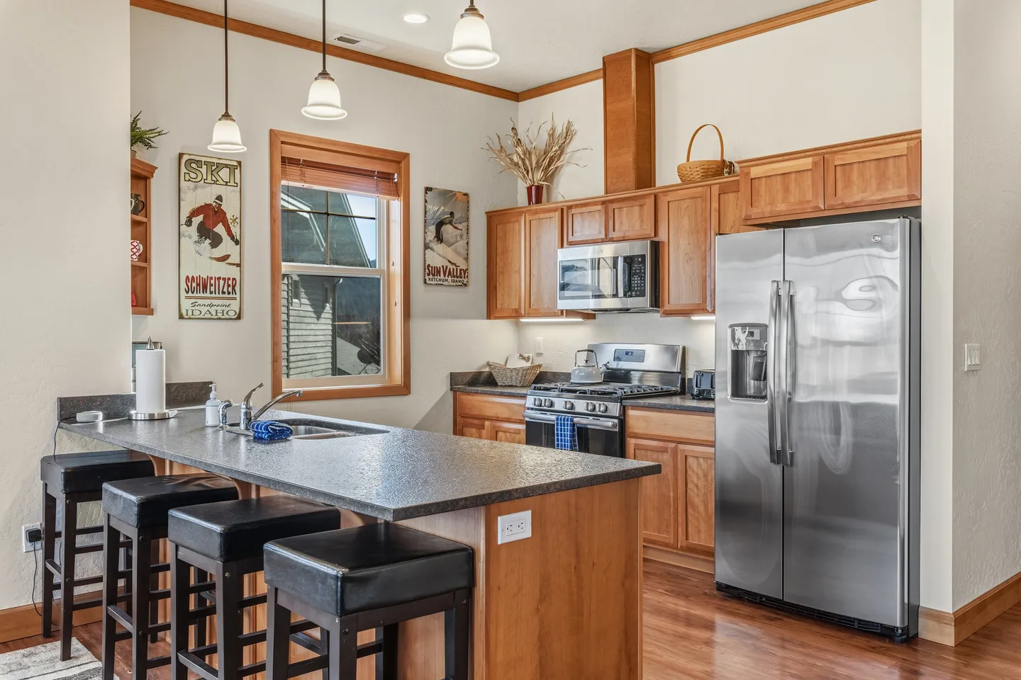 A kitchen with wooden cabinets, stainless steel appliances, a peninsula counter with bar stools, and ski-themed wall art.