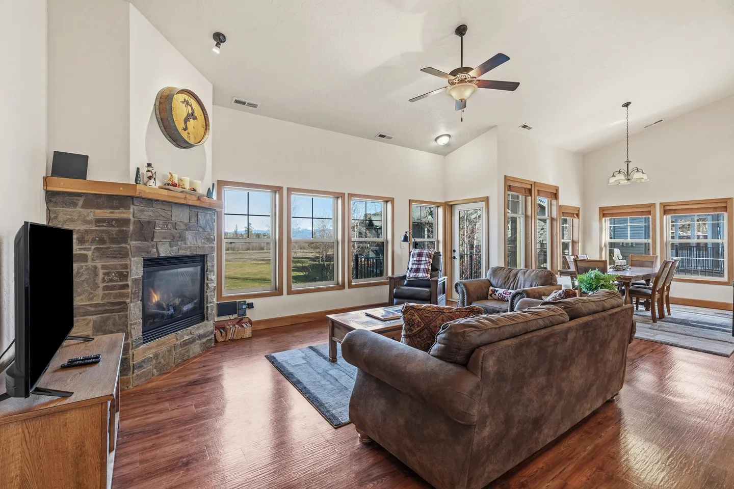 Living room with a stone-clad fireplace, sofas, television, and large windows looking outside.