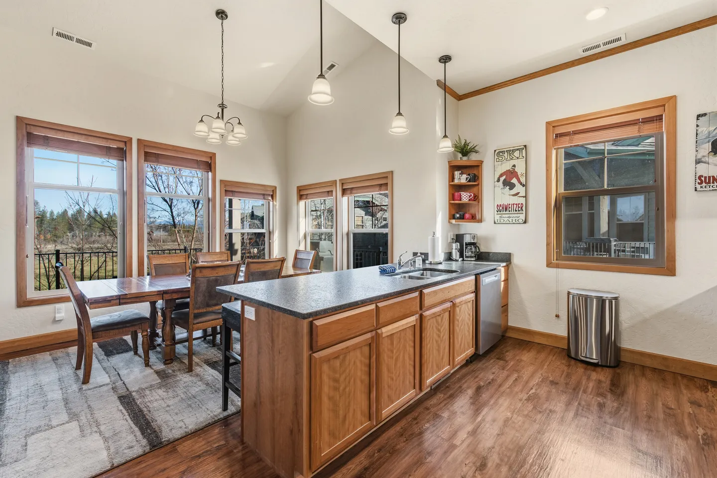 Open-concept dining area and kitchen island with wooden cabinets, dark countertops, wood-style flooring, and large windows.