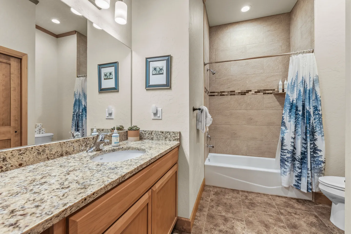 Bathroom with granite vanity countertop, large mirror, and tiled shower tub combo with tree-patterned curtain.