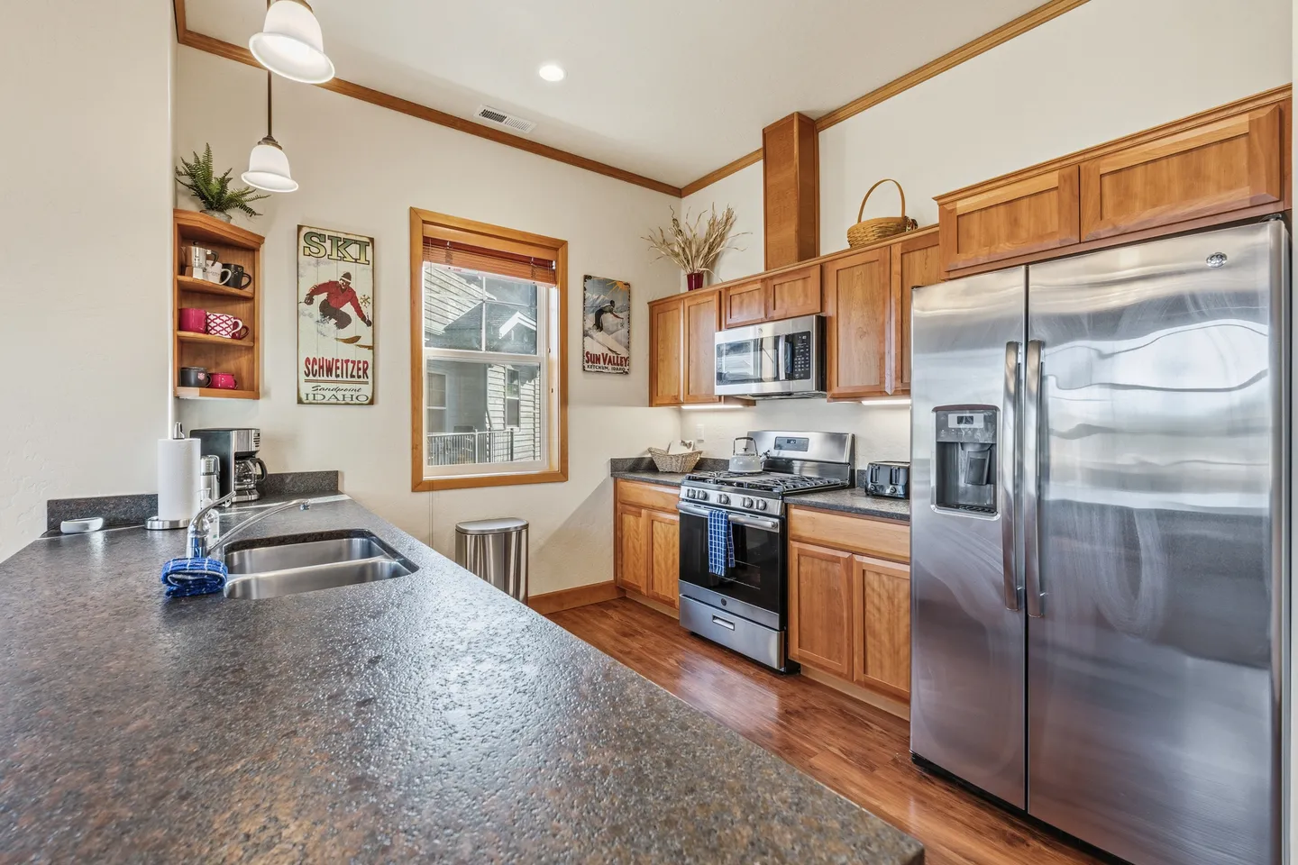Kitchen interior featuring dark countertops, light wood cabinets, stainless steel appliances, and ski-themed wall art.