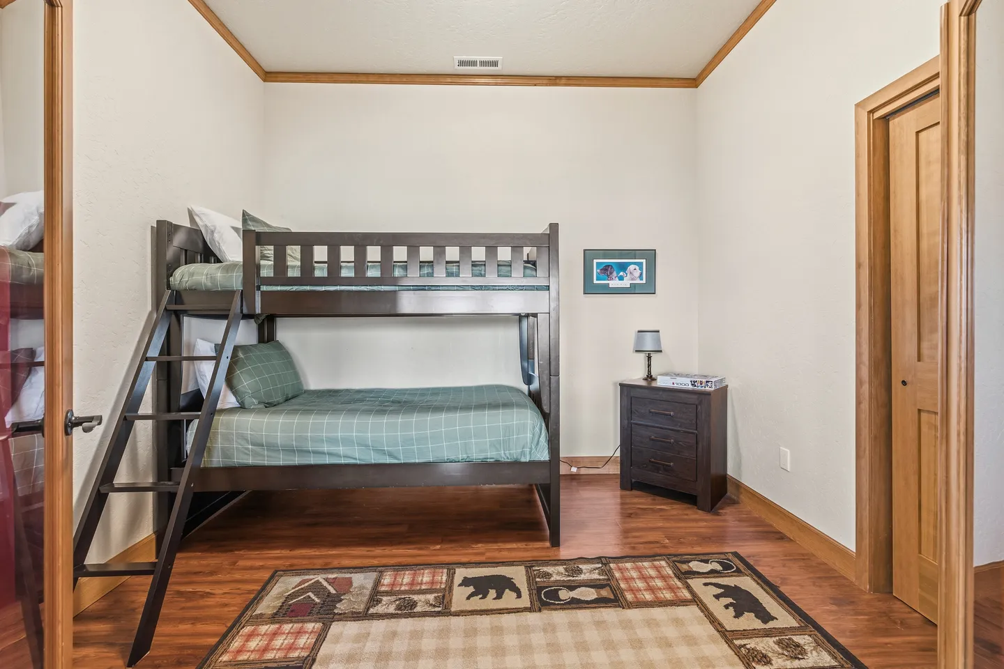 Bedroom featuring a dark wood bunk bed with green plaid bedding, a matching nightstand, and a rustic themed area rug on wood-look flooring.