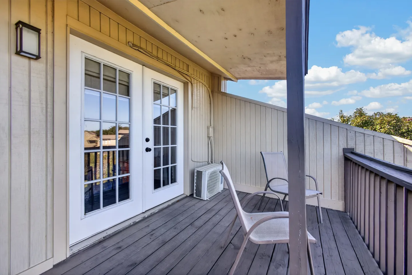 Outdoor balcony with grey wooden decking, white french doors, and two patio chairs under a covered overhang.