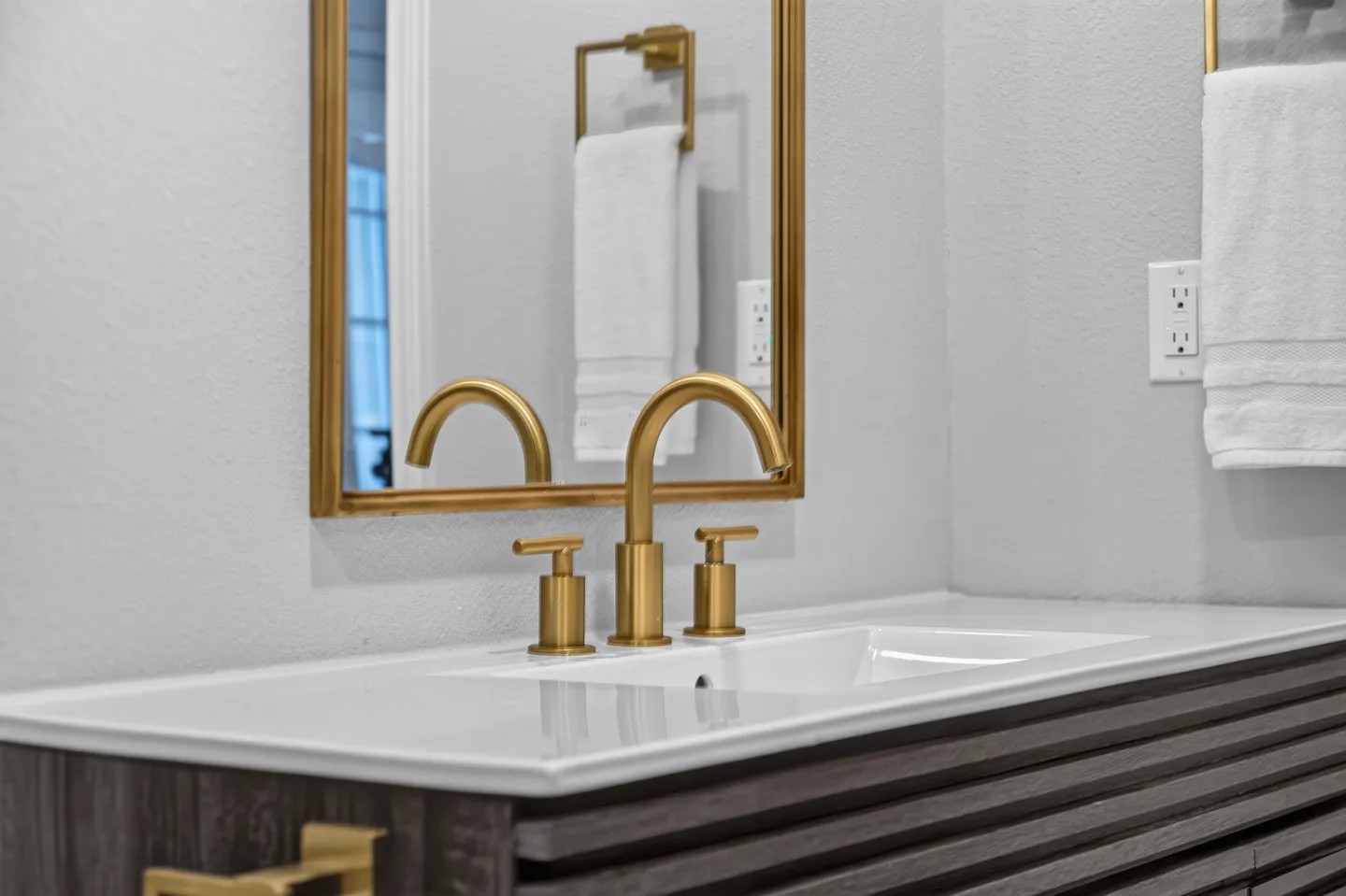 Close-up of a bathroom vanity featuring a white sink countertop, gold-toned faucet, and a gold-framed mirror.