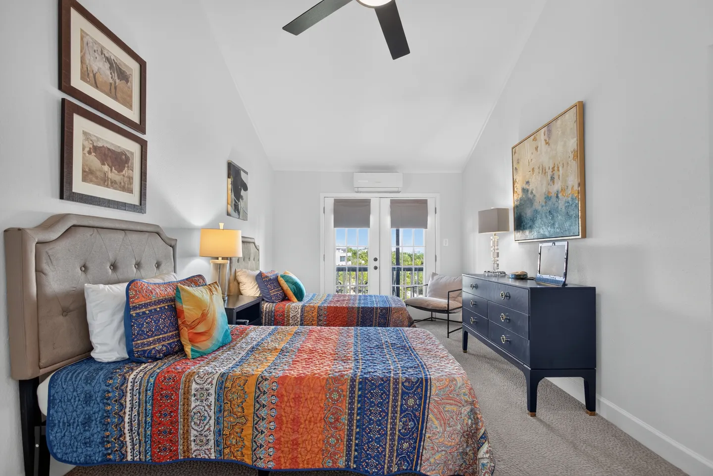 Bedroom with two twin beds dressed in colorful patterned bedding, a dark blue dresser, and glass doors leading to a balcony.