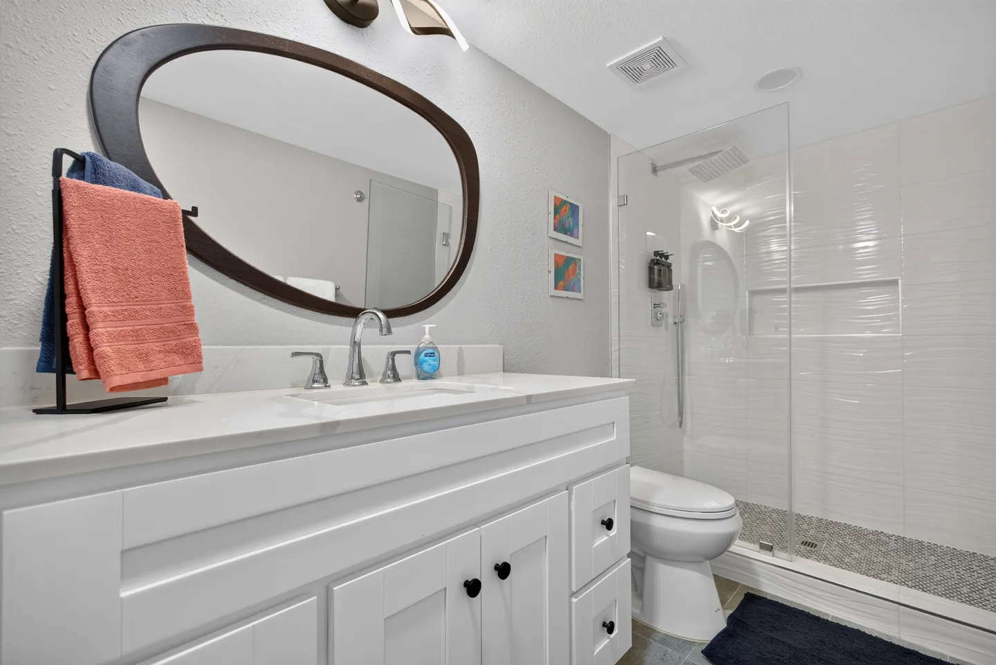 Bathroom featuring a white vanity with an oval mirror, a toilet, and a glass-enclosed walk-in shower with tiled walls.