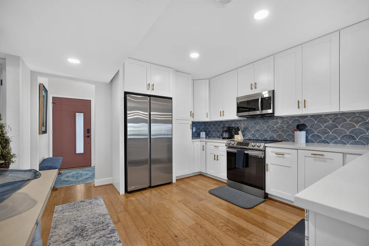 Bright kitchen with white cabinets, stainless steel appliances, blue scalloped tile backsplash, and light wood flooring.